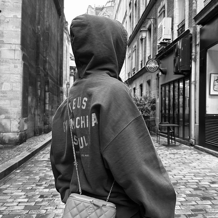 a person in a hoodie is walking down the street with a handbag on his shoulder