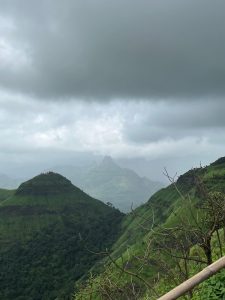 Misty green mountain valley beneath dramatic dark clouds, with a rugged peak rising in the distant landscape.